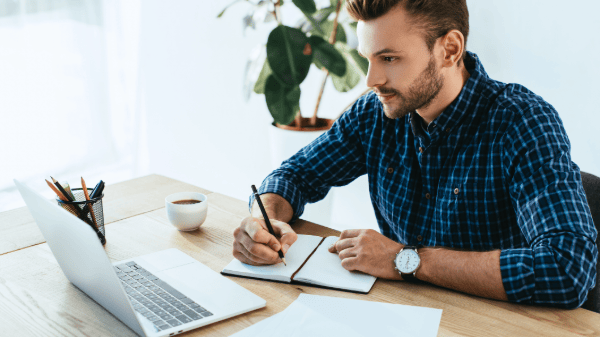 Broker reviewing compliance guidelines on his laptop and taking notes.
