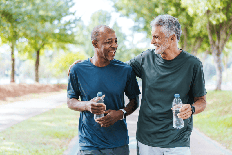 Senior friends walking in public park, holding bottles of water.