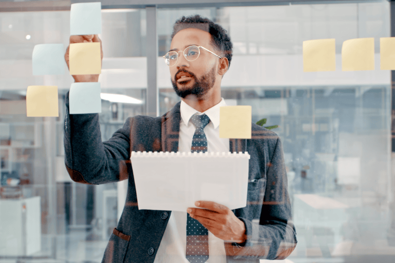 Person in a suit writing on sticky notes on a glass wall in an office