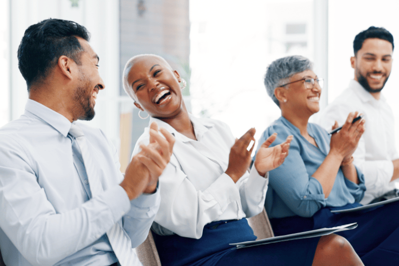 Four people sitting down clapping in business attire