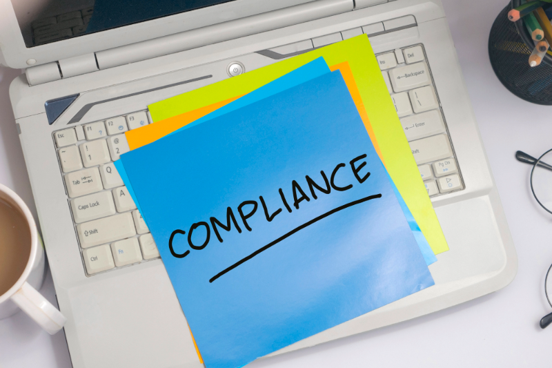 Post-it note with "Compliance" written on it while it is on the keyboard of a laptop