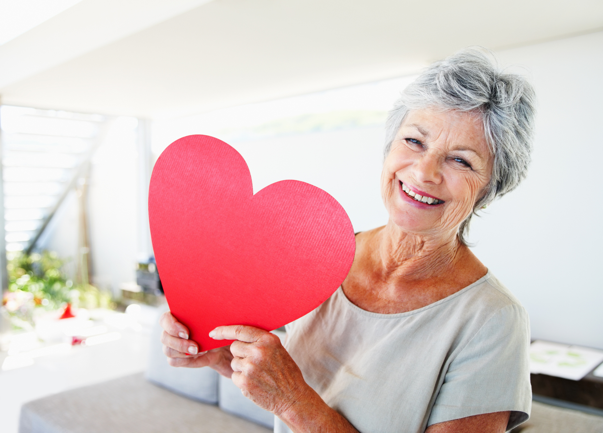Senior woman smiling and holding a large cut out heart