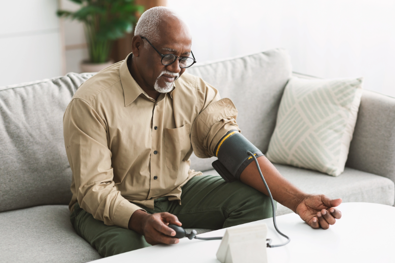 Senior man sitting on a couch taking his blood pressure