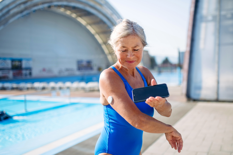 Older woman standing by a pool checking her glucose with her phone