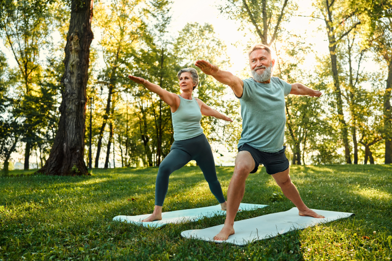 A senior man and senior woman in the park doing yoga on yoga mats