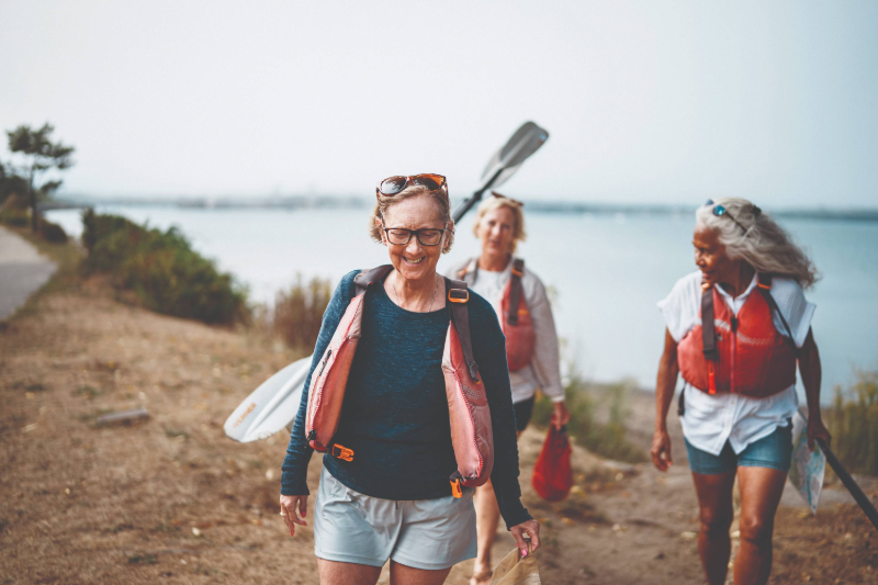 Three senior women walking with paddles by the water