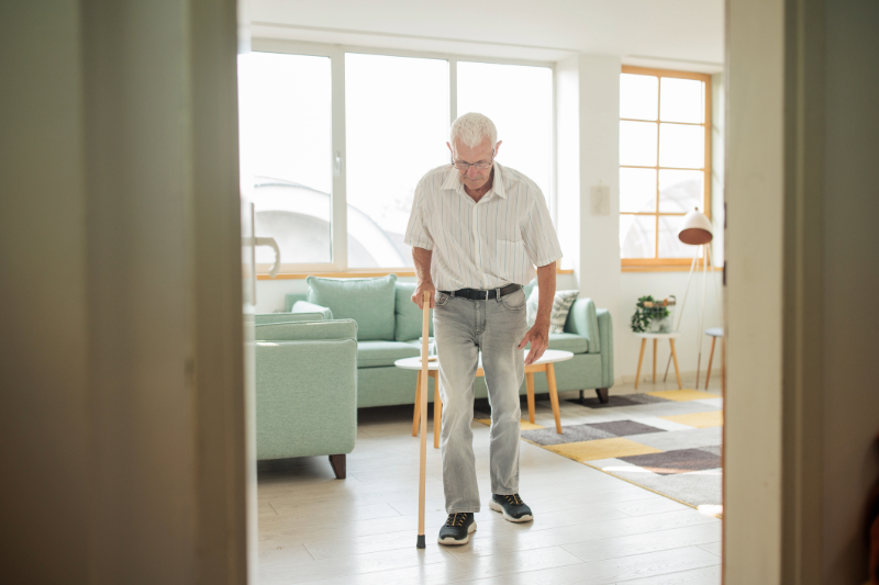 Senior man using a cane to walk through the house