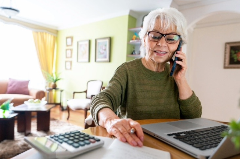 Senior woman sitting at a table on the phone in front of a laptop