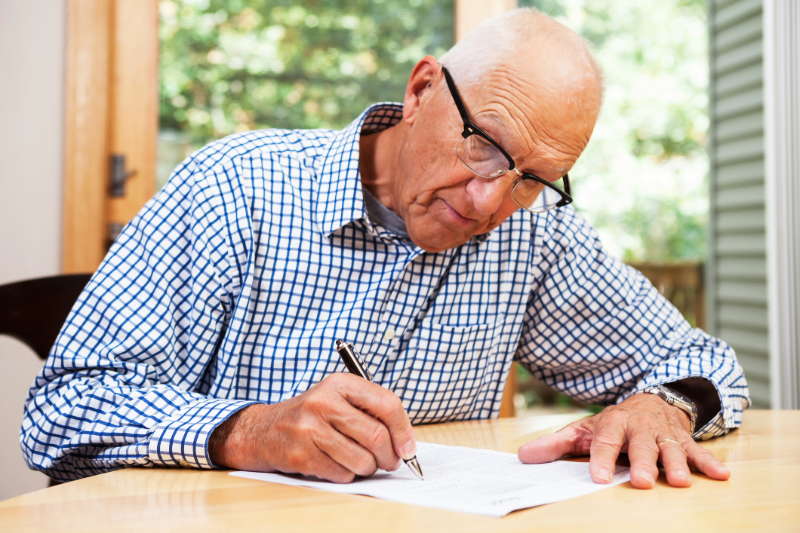 Senior man sitting at a table writing on paper
