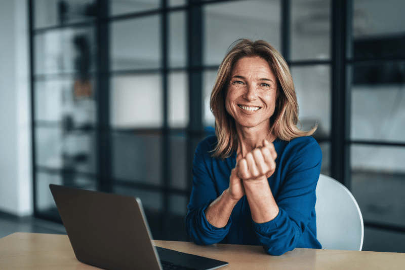 Business woman in the office, smiling, at a desk with a laptop.